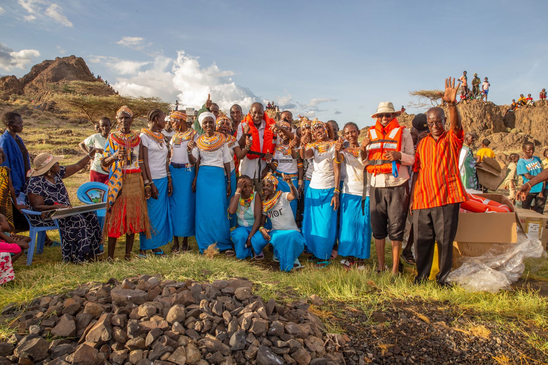 Group in traditional blue and orange dress with mountains behind.