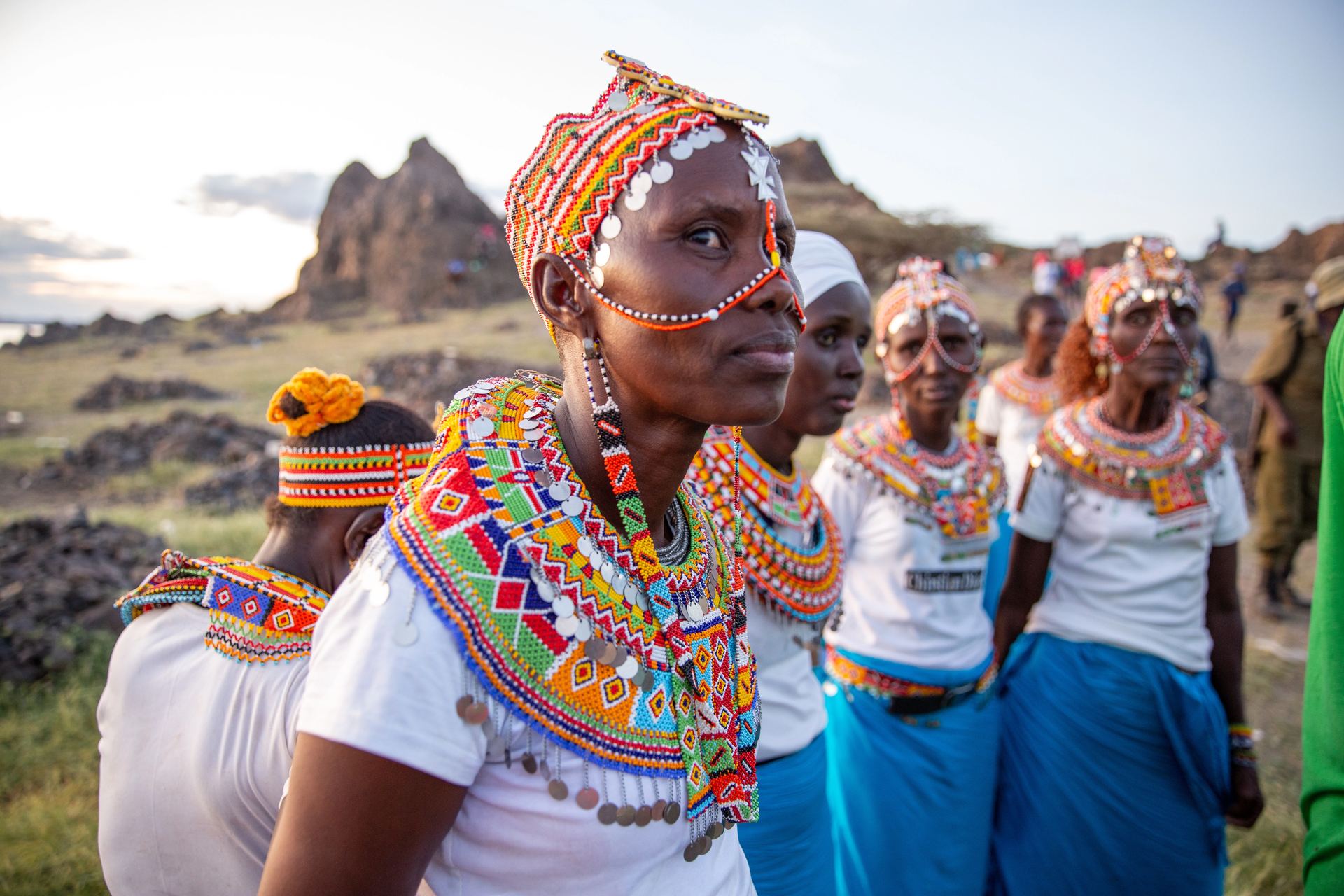Women in white and blue traditional dress against a mountain backdrop.